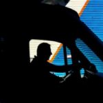 Silhouette of a commercial truck driver in front of a blue side panel of a background truck.