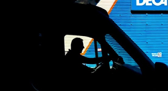 Silhouette of a commercial truck driver in front of a blue side panel of a background truck.