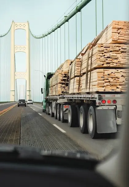 Stylized graphic of an oversized load of wood on a flatbed truck driving over a bridge.