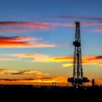 Oil drilling rig silhouetted against a fiery sunset sky