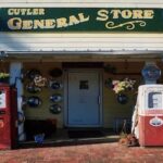 Two vintage gas pumps, one red Phillips 66 and one white and red, outside the Cutler General Store, whose porch walls are decorated with old hubcaps.