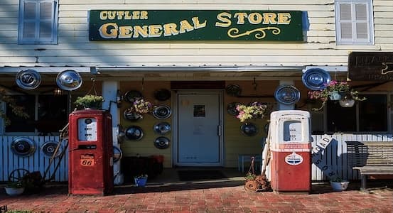 Two vintage gas pumps, one red Phillips 66 and one white and red, outside the Cutler General Store, whose porch walls are decorated with old hubcaps.