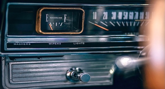 Close-up of a vintage car dashboard with the fuel gauge needle near empty, a chrome-trimmed speedometer, and switches labeled washers, wipers, and lights.